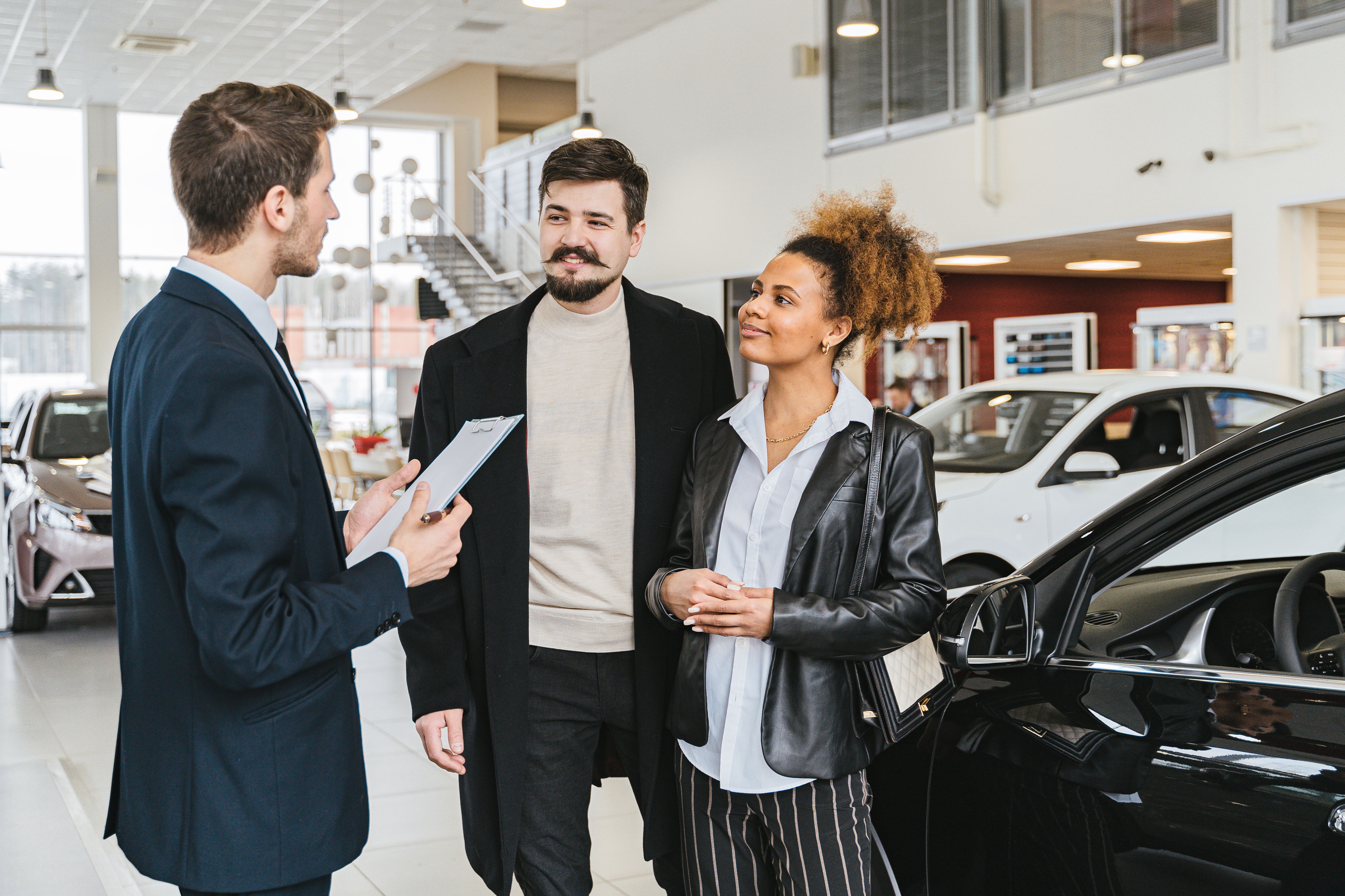 Vendedor de una concesionaria porteña explicando opciones de financiación y planes de ahorro a una pareja frente a un auto 0km